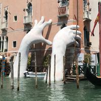 Large hand sculpture reaching out from water to hold building