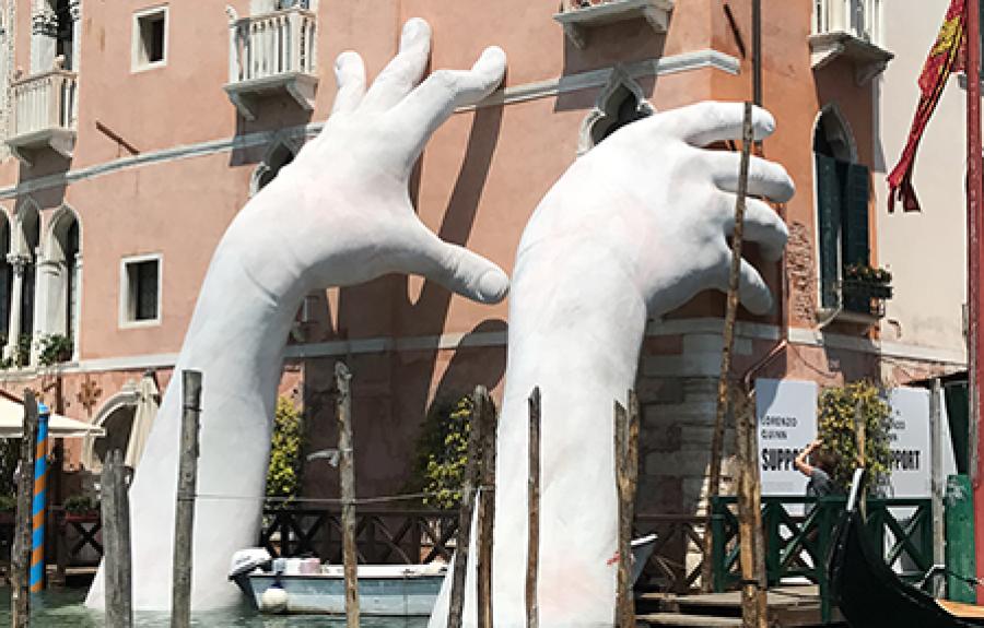 Large hand sculpture reaching out from water to hold building